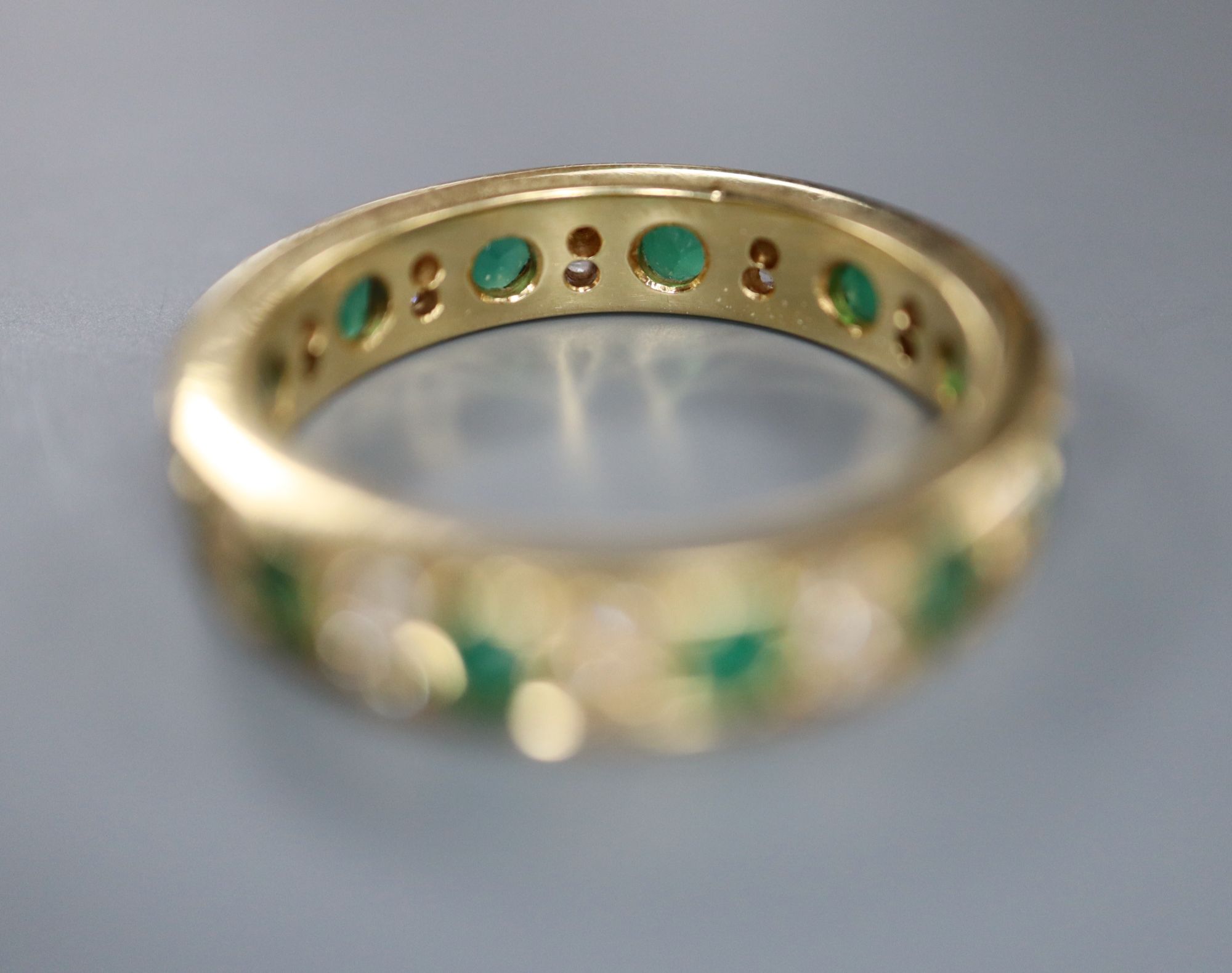 A mid to late 20th century yellow metal, emerald and diamond set full eternity ring, size P/Q, gross 5.7 grams.